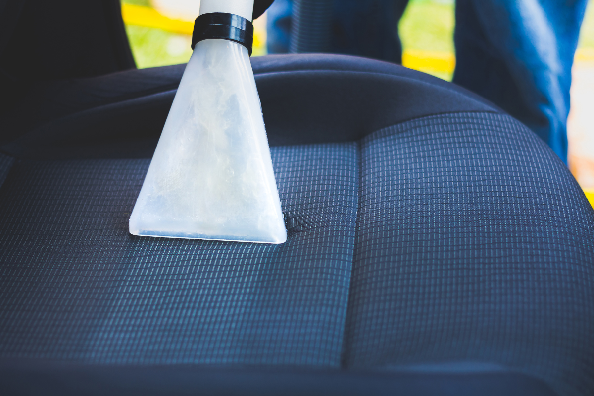 A professional car upholstery cleaning, their machine runs over a deep blue car seat, revealing a lighter blue strip underneath the grime.